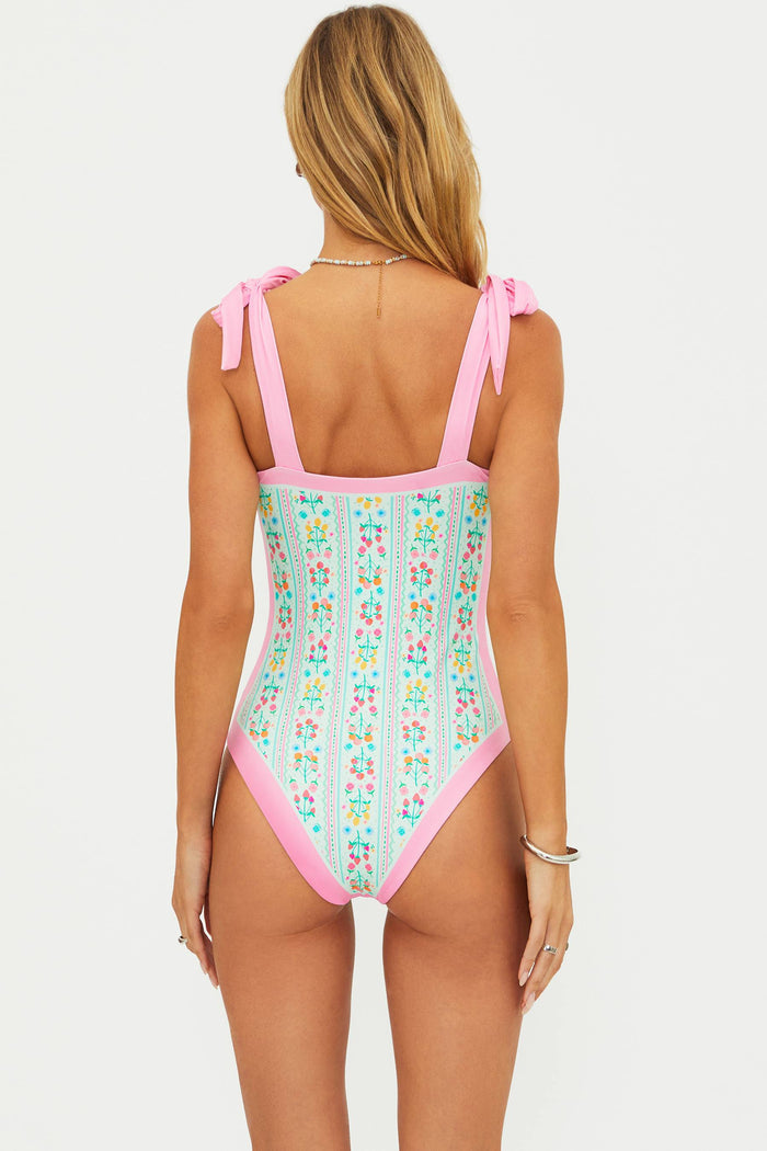 Woman wearing a floral one-piece swimsuit with pink straps on a white background