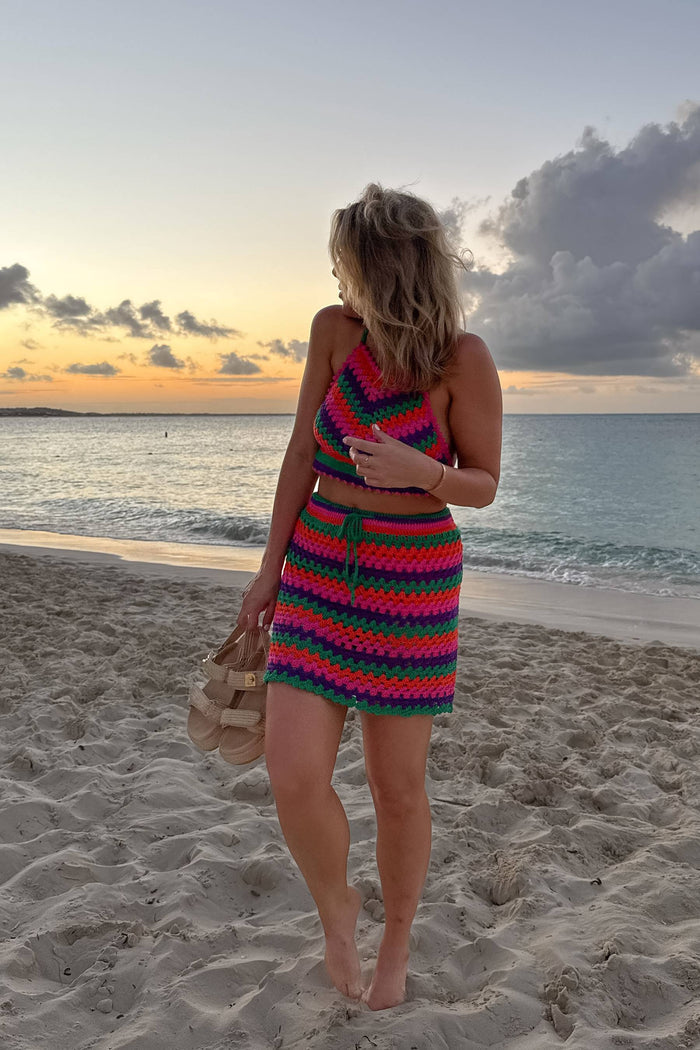 Woman in colorful crochet outfit standing on a beach at sunset