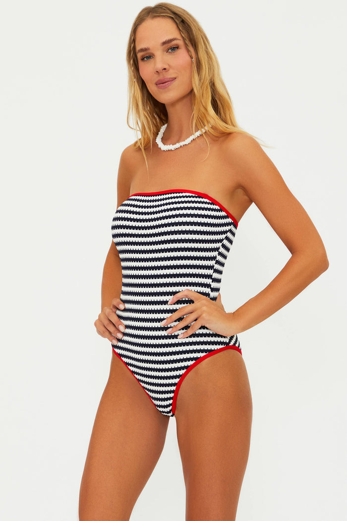 A strapless one-piece swimsuit in indigo and white stripes with moderate coverage and high leg cut. Model is wearing a small size.
