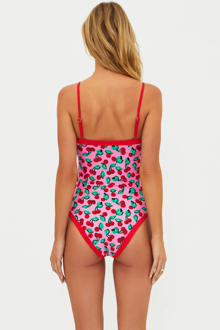 Woman wearing a strapless one piece with pink and red cherries. There are red adjustable straps on the one piece.