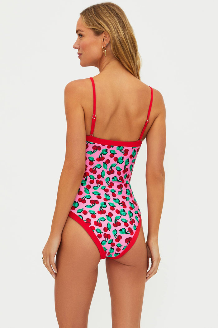 Woman wearing a strapless one piece with pink and red cherries. There are red adjustable straps on the one piece.