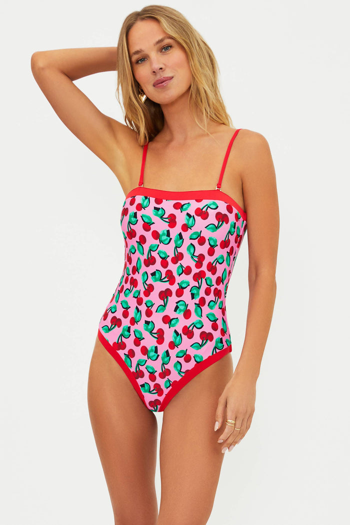 Woman wearing a strapless one piece with pink and red cherries. Wearing red adjustable straps on the one piece.