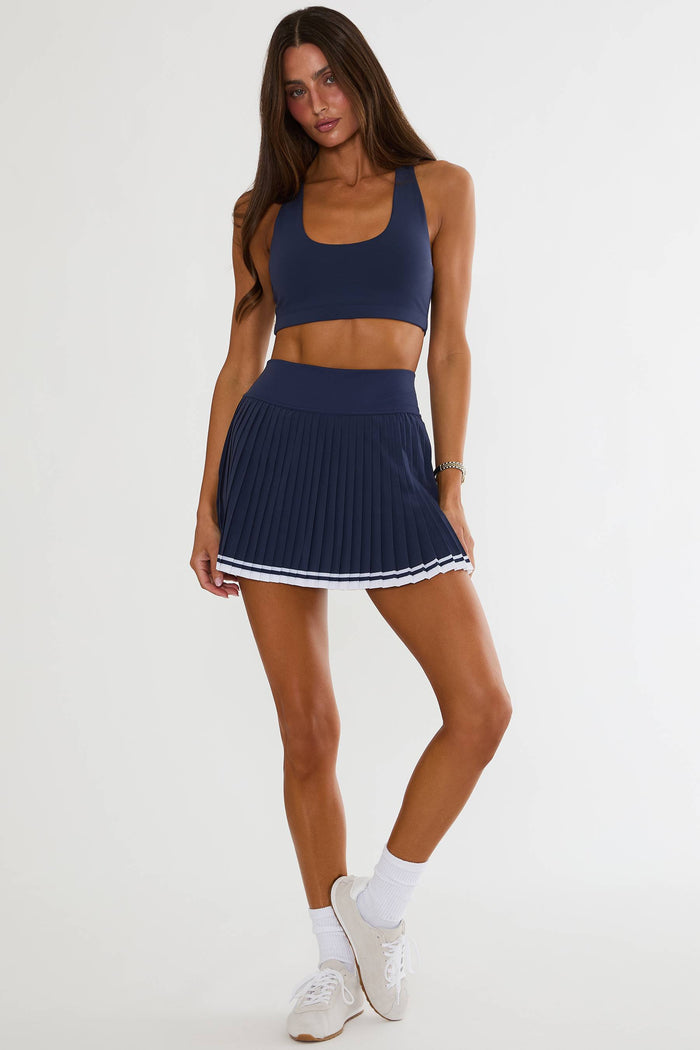 Person wearing a navy blue athletic outfit with a skirt on a white background