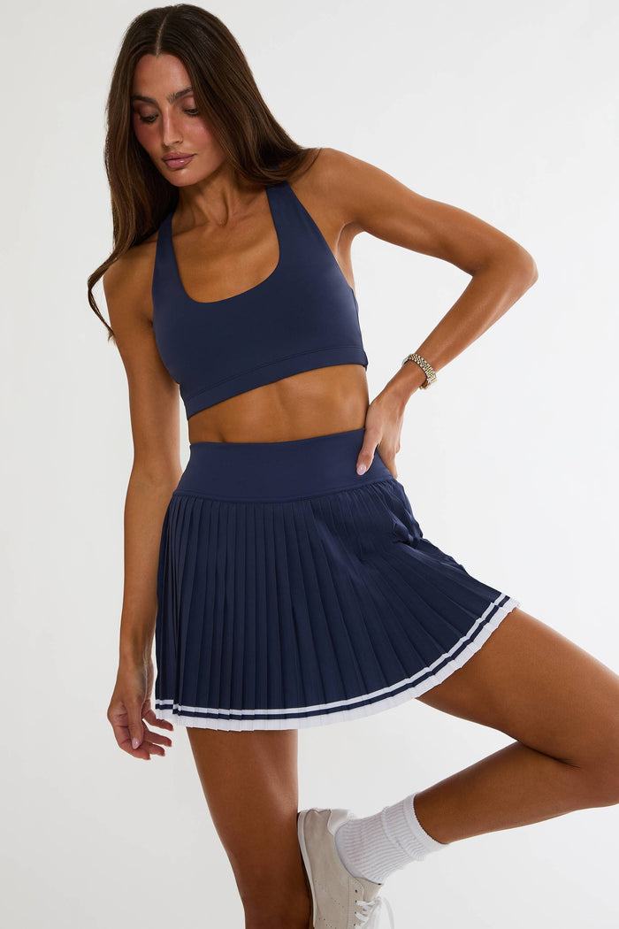 Woman wearing a navy blue sports bra and skirt set on a white background