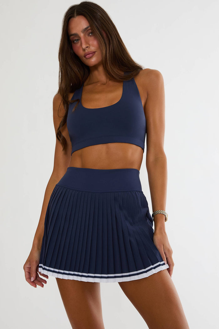 Woman wearing a navy blue sports bra and skirt set on a white background