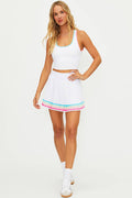 Woman wearing a white tennis skirt with colorful lining along the bottom on a  white wall.