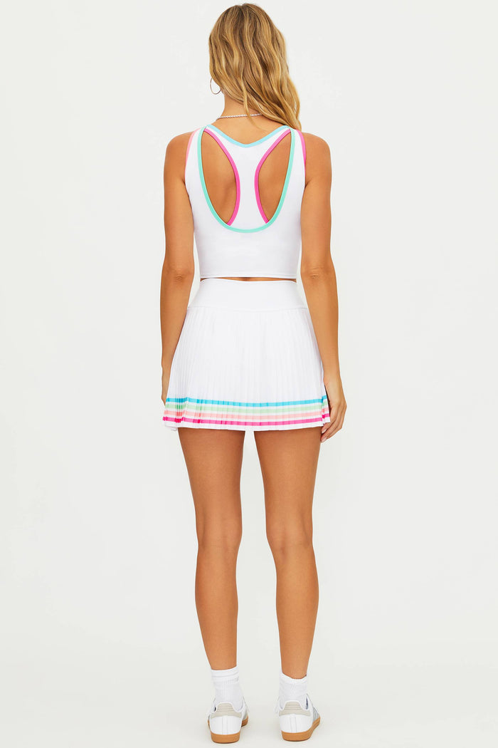 Woman wearing a white tennis skirt with colorful lining along the bottom on a  white wall.