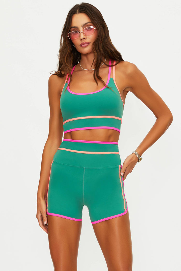 Woman wearing a green sports bra with colorful lining on a white wall.