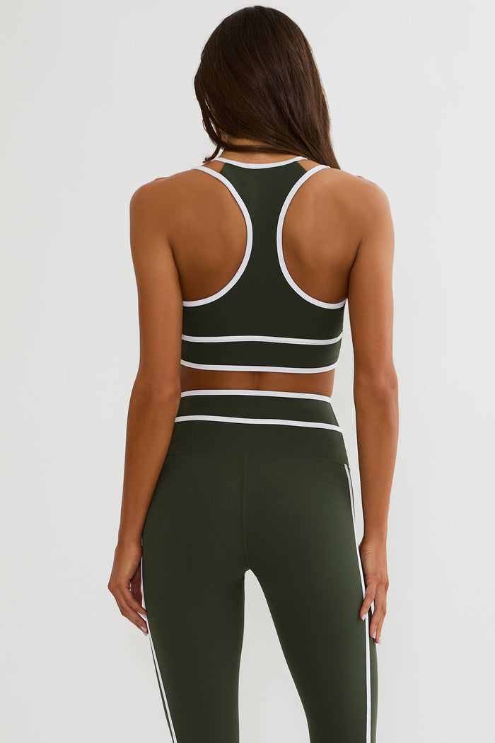 A woman shown from the back wearing an olive green athletic set with white trim, including a sports bra and high-waisted leggings, against a light gray studio background.