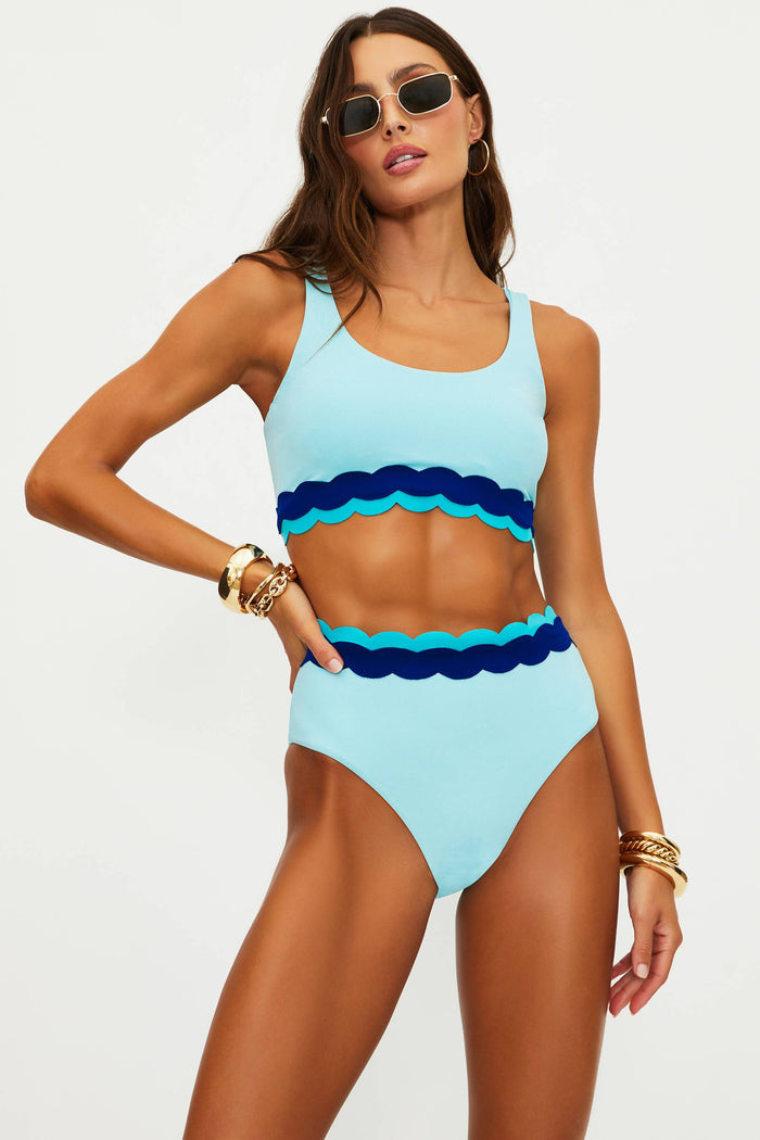 Woman wearing a blue and navy scalloped bikini set on a white background