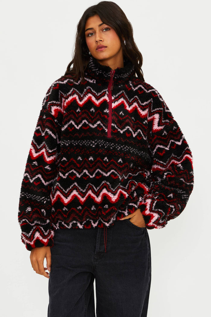 Person wearing a patterned sweater with red and white design on a plain background