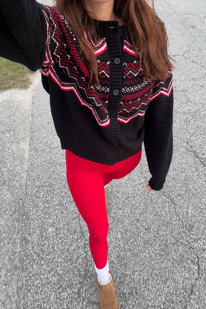Person wearing a black and red patterned cardigan with red leggings on a gray pavement.