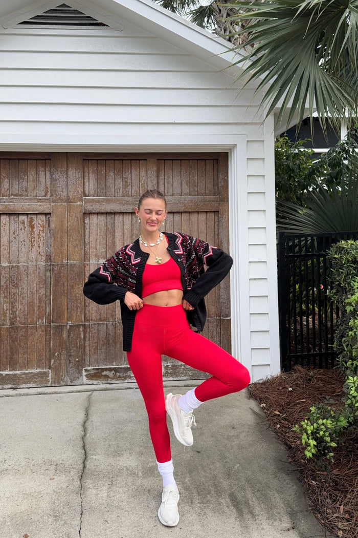 Person in red leggings and black jacket posing in front of a white house.