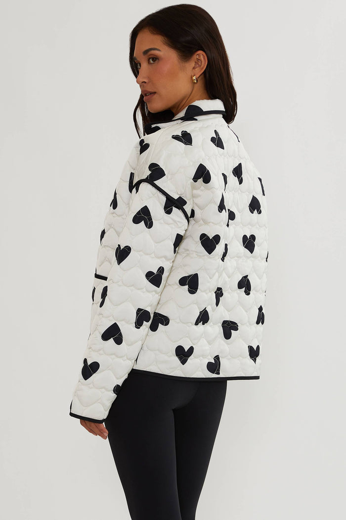 Person wearing a white puffer jacket with black heart patterns on a plain background