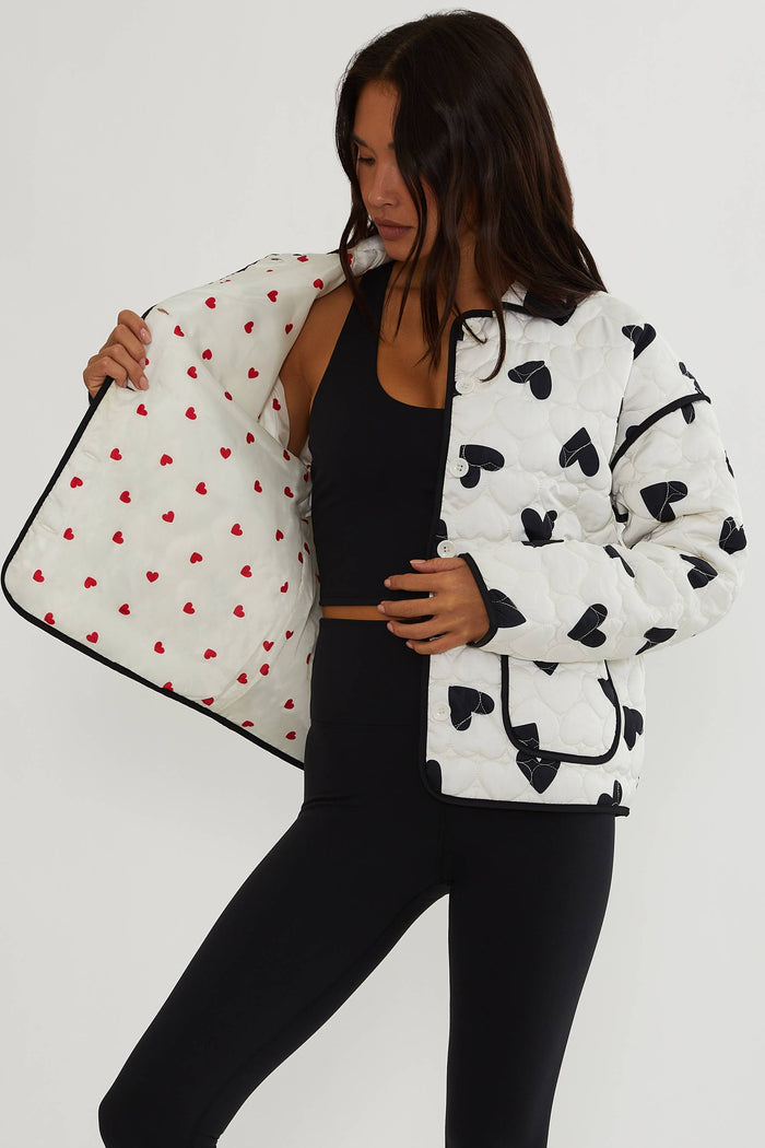 Woman holding a polka dot bag wearing a black and white patterned jacket on a white background