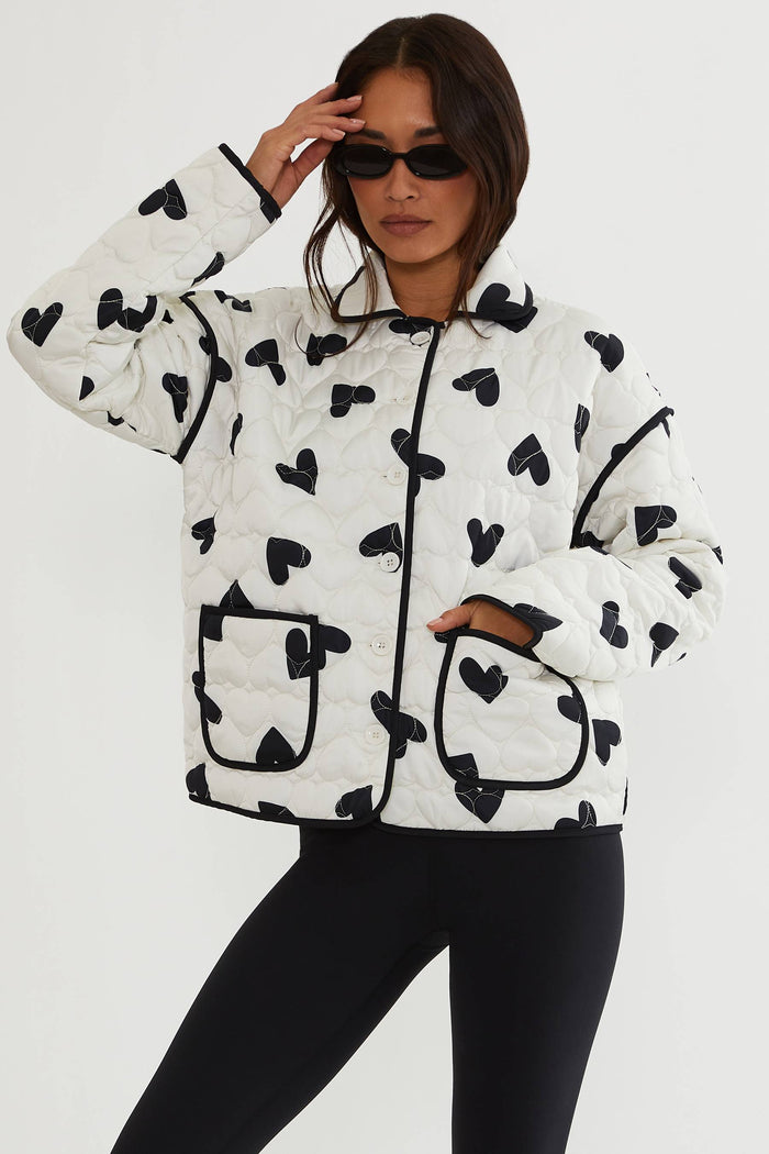 Person wearing a white jacket with black heart patterns on a plain background