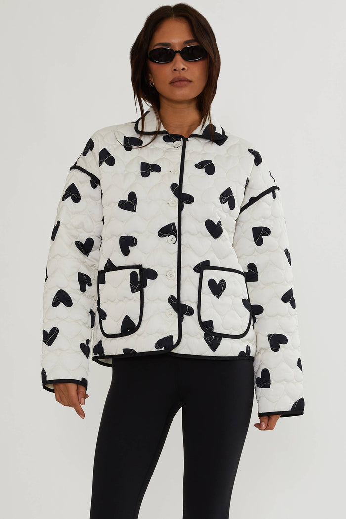 Person wearing a white puffer jacket with black heart patterns on a white background