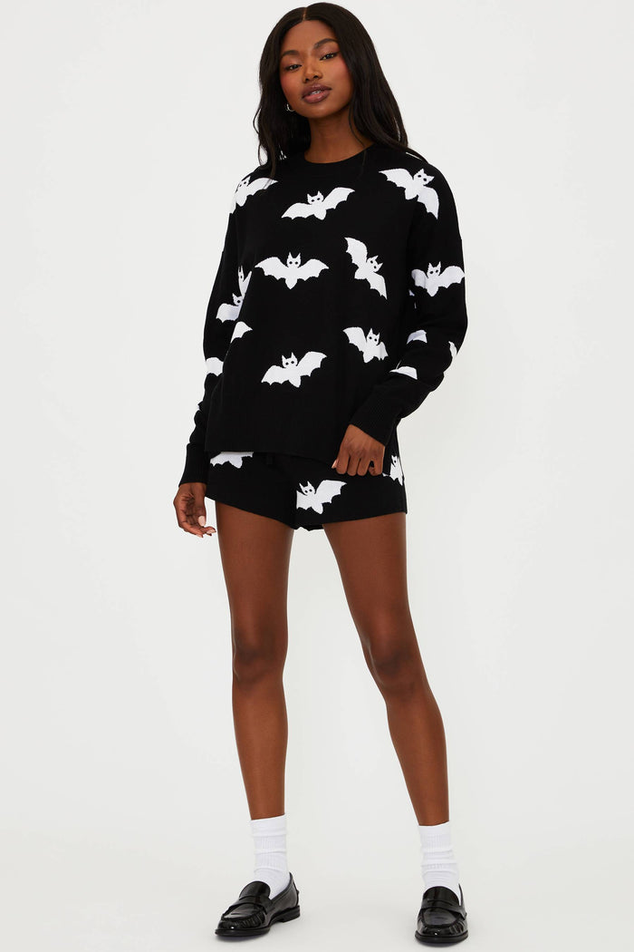 Person wearing a black sweater with white bat patterns on a white background
