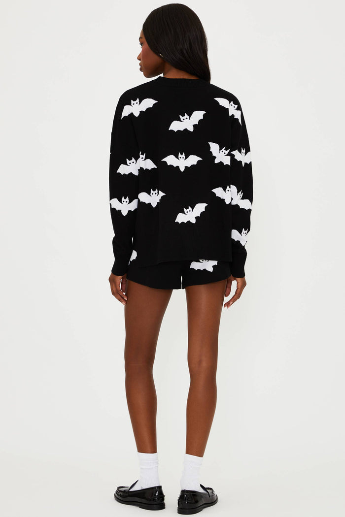 Person wearing a black sweater with white bat patterns on a white background