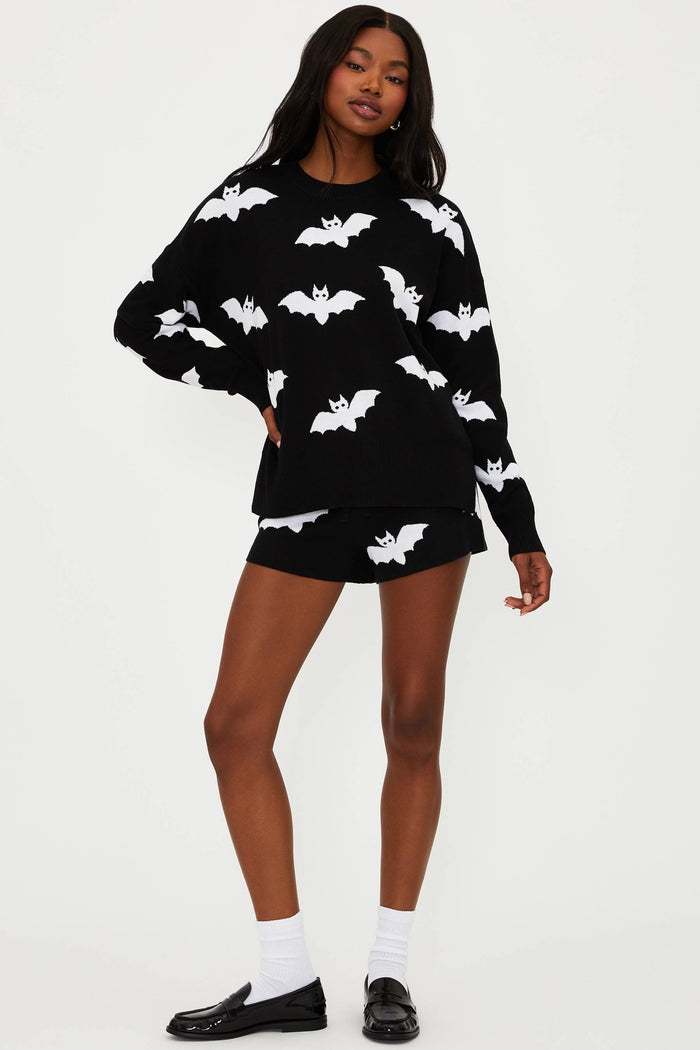 Person wearing a black sweater with white bat patterns and black shorts on a white background