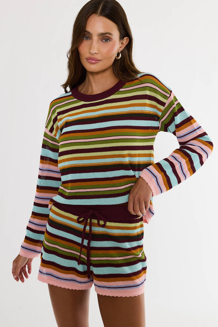A woman modeling a ribbed knit two-piece loungewear set featuring a long-sleeve top and matching shorts with horizontal multicolor stripes in shades of green, orange, blue, pink, brown, and burgundy.