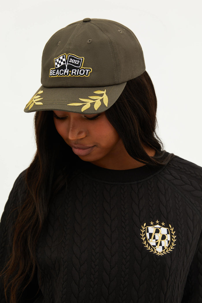 An olive green dad hat with the Beach Riot logo on the front and decorative yellow embroidery on the sides.