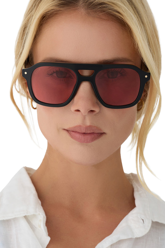 Woman wearing black sunglasses with red lenses on a white background