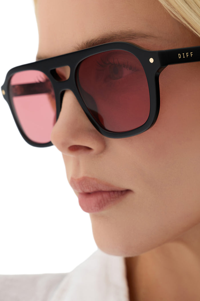 Close-up of a person wearing black sunglasses with pink lenses.
