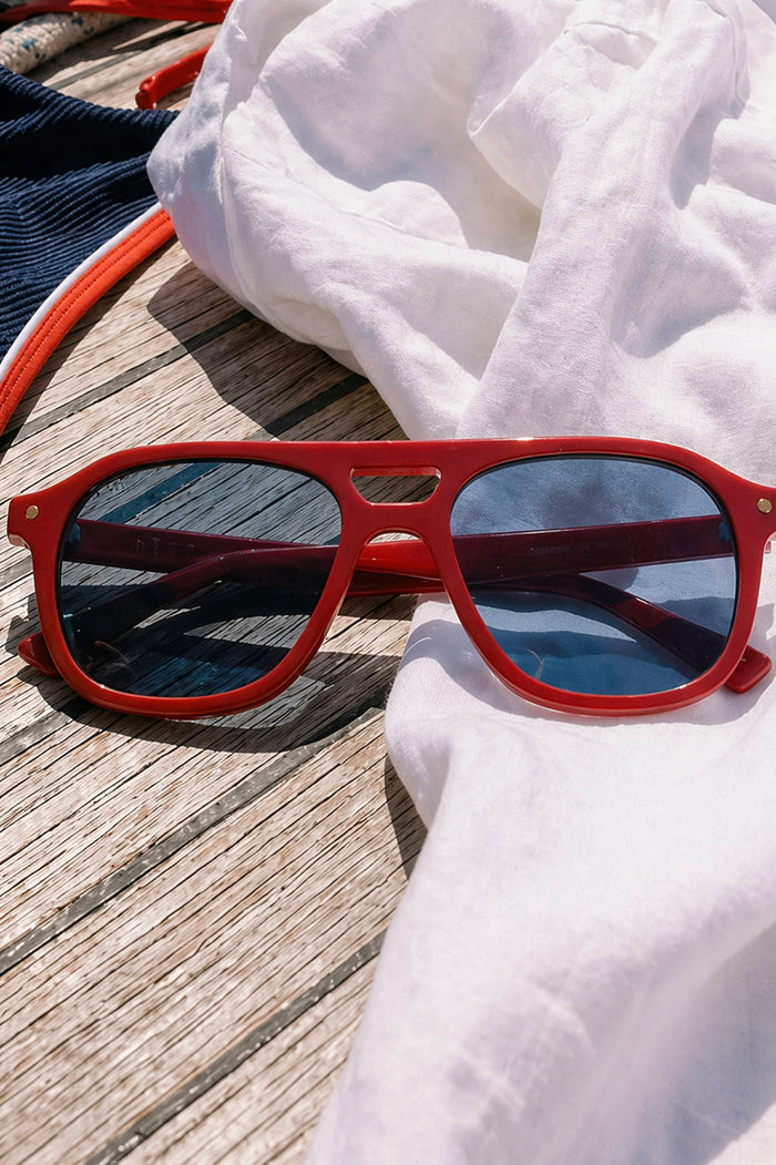 Red sunglasses with blue lenses on a white towel on a wooden surface