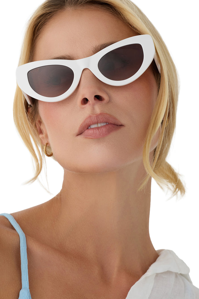 Woman wearing white cat-eye sunglasses with a plain background