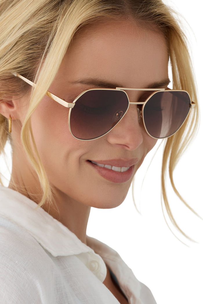 Woman wearing gold-framed sunglasses with a blurred white background