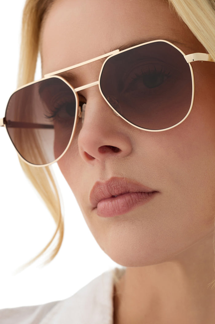 Close-up of a person wearing gold-framed sunglasses with a neutral background