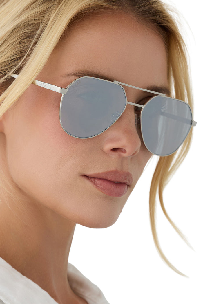Close-up of a person wearing silver sunglasses with a neutral background