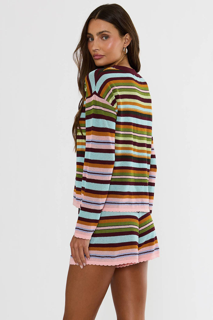 A woman modeling a matching striped knit long-sleeve top and shorts set. The set features horizontal stripes in pink, light blue, olive green, mustard yellow, brown, and dark burgundy, with a solid dark burgundy crew neck and drawstring waist.