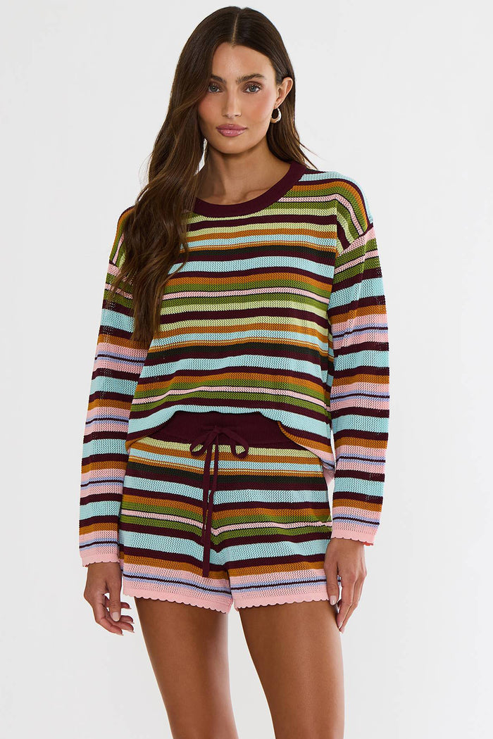 A woman modeling a matching striped knit long-sleeve top and shorts set. The set features horizontal stripes in pink, light blue, olive green, mustard yellow, brown, and dark burgundy, with a solid dark burgundy crew neck and drawstring waist.