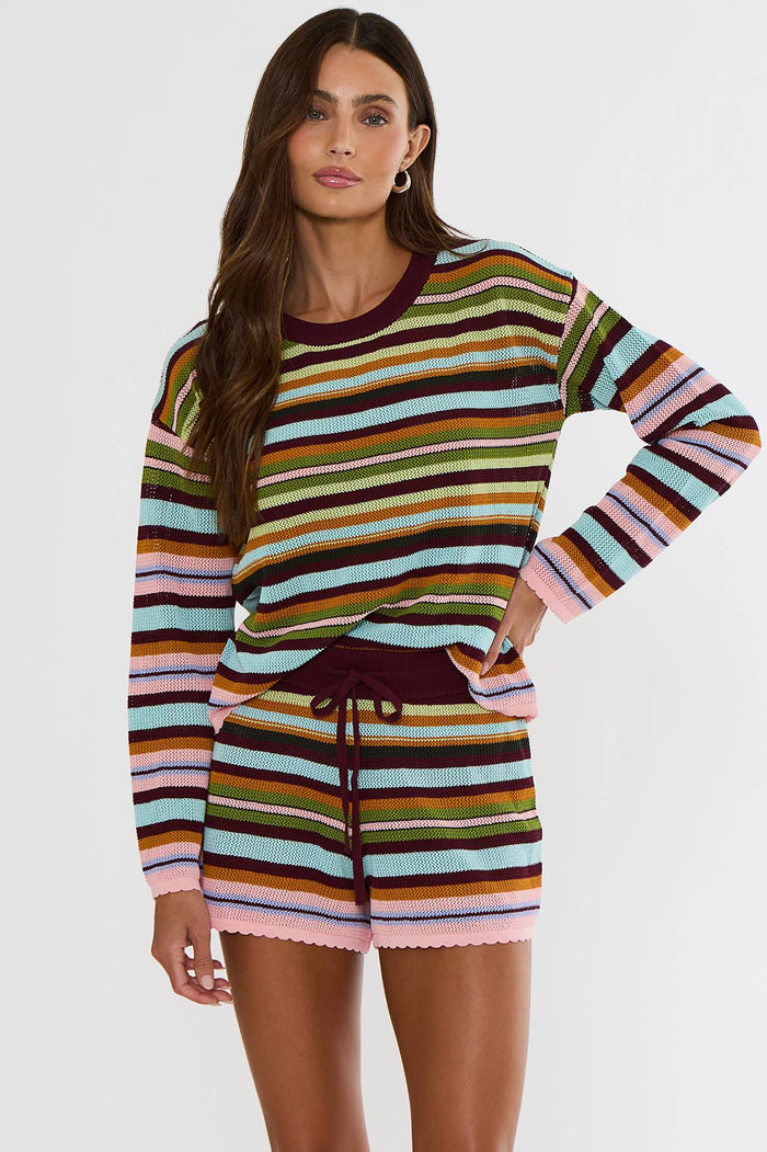 A woman modeling a matching striped knit long-sleeve top and shorts set. The set features horizontal stripes in pink, light blue, olive green, mustard yellow, brown, and dark burgundy, with a solid dark burgundy crew neck and drawstring waist.