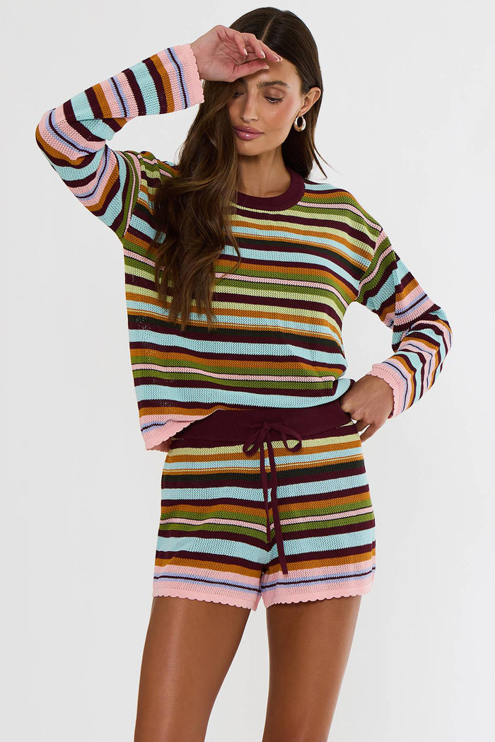 A woman modeling a matching striped knit long-sleeve top and shorts set. The set features horizontal stripes in pink, light blue, olive green, mustard yellow, brown, and dark burgundy, with a solid dark burgundy crew neck and drawstring waist.