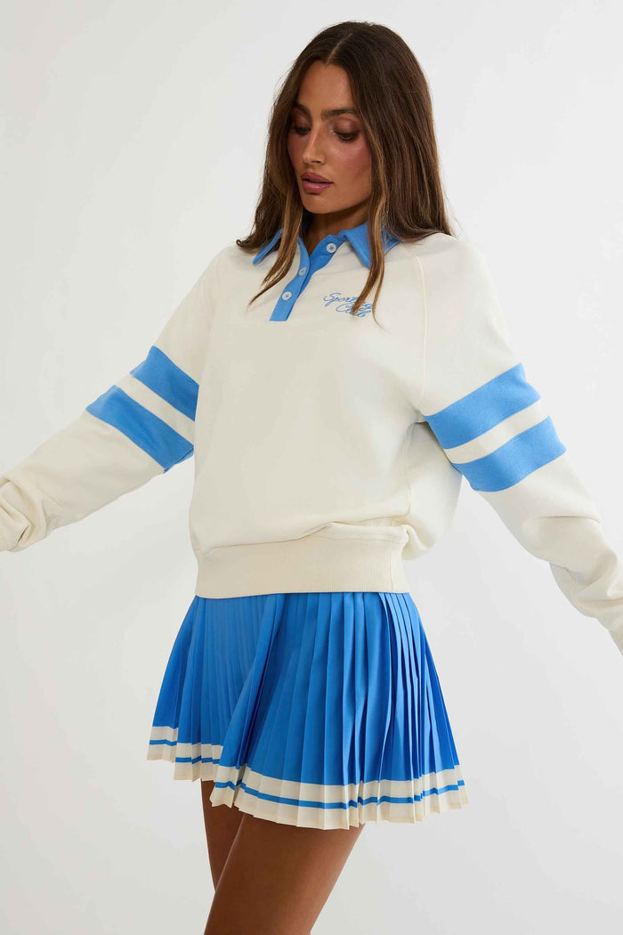 Woman wearing cream and blue polo sweater with "sports club" text on the chest.