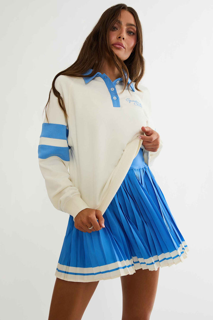 Woman wearing cream and blue polo sweater with "sports club" text on the chest.
