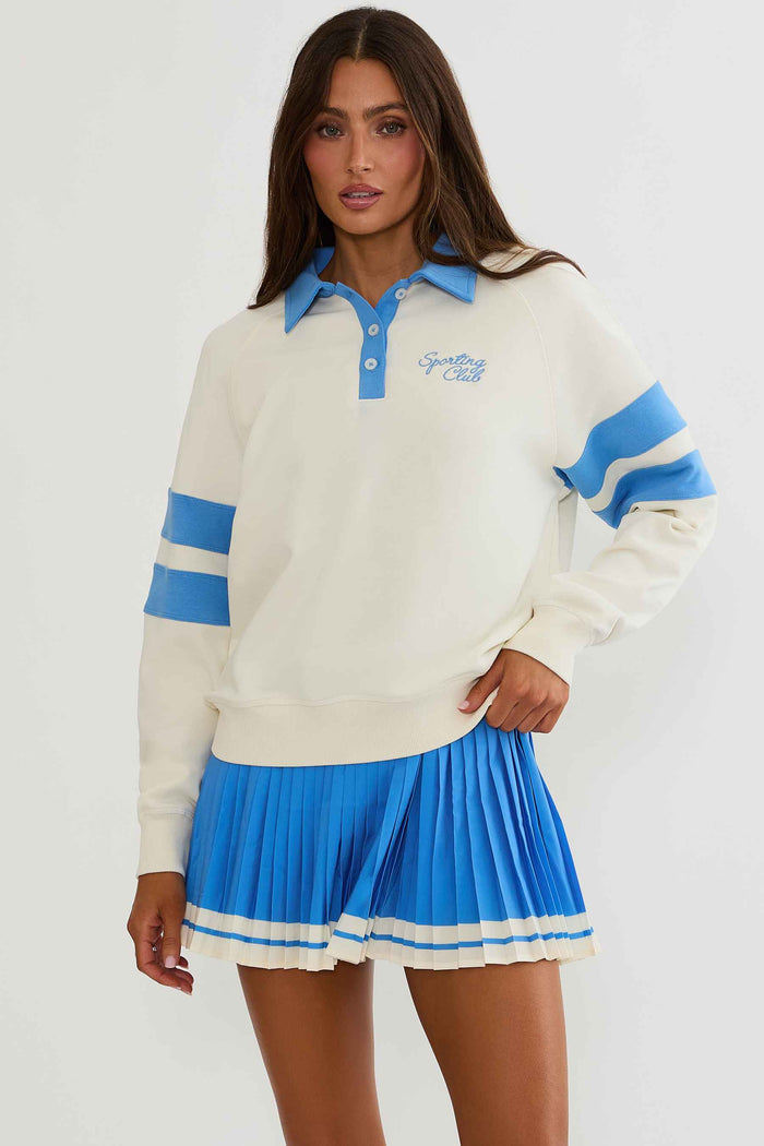 Woman wearing cream and blue polo sweater with "sports club" text on the chest.