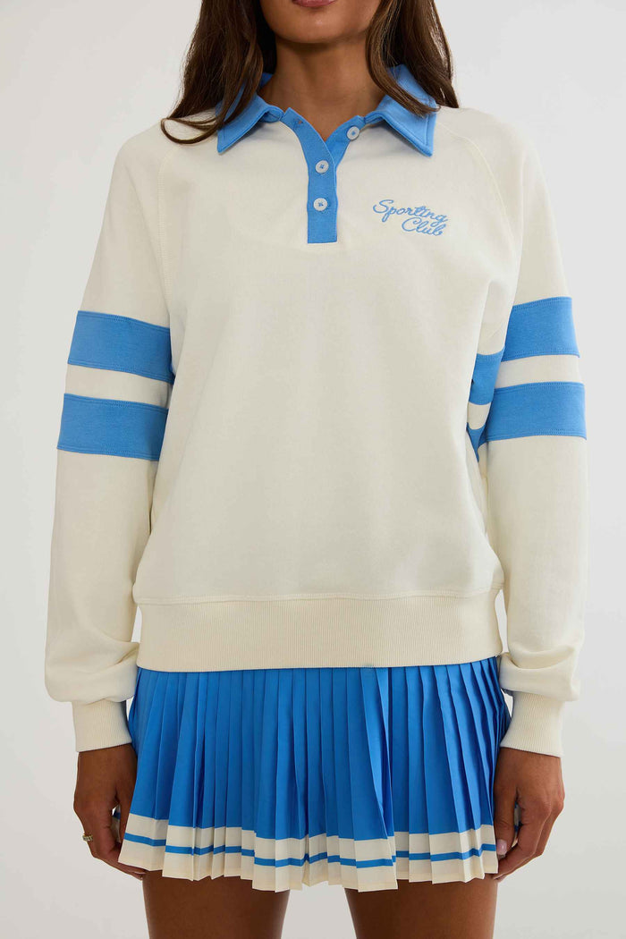 Woman wearing cream and blue polo sweater with "sports club" text on the chest.