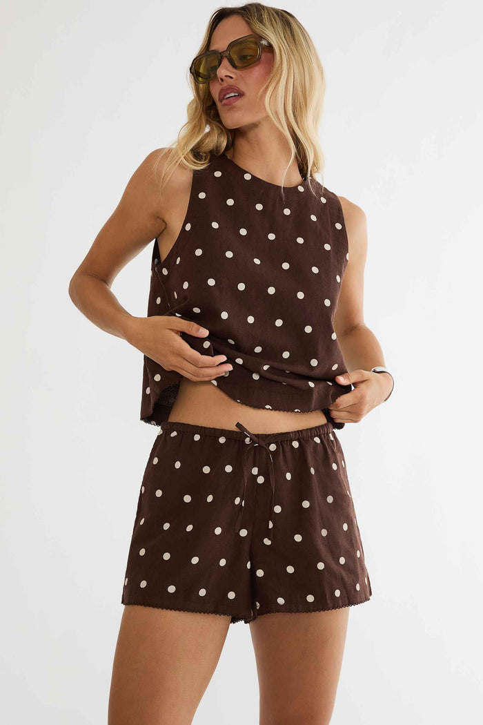 Woman wearing a brown polka dot outfit with sunglasses on a white background