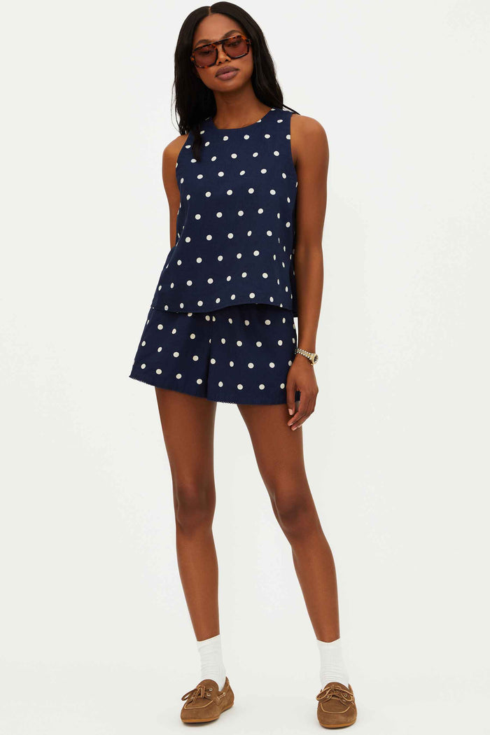 A model wearing navy shorts with white polka dots, a drawstring waistband, and side pockets.