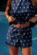 A model wearing navy shorts with white polka dots, a drawstring waistband, and side pockets.
