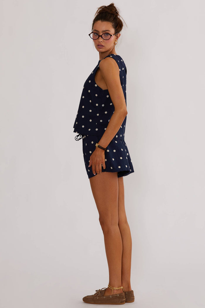 A model wearing navy shorts with white polka dots, a drawstring waistband, and side pockets.