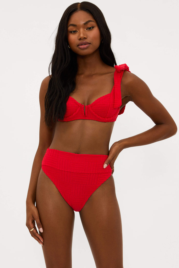 This image features the Blair Top Cherry Terry, a stylish and supportive swimwear top. Modelled by a woman showcasing a serious expression, the top is presented in a vivid cherry red color.