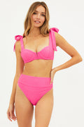 A woman wearing a pink textured jacquard fabric swim top with a sweetheart neckline and self-tie shoulders.