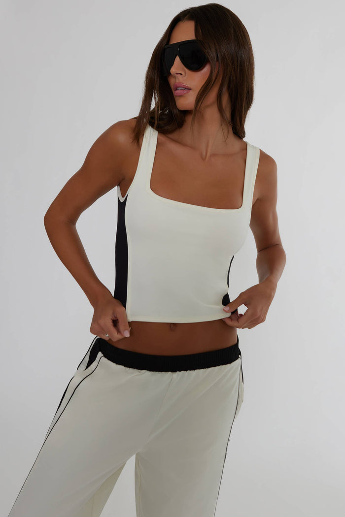 A woman modeling a white crop top with black side panels and matching white jogger pants with black side stripes, photographed against a light gray studio background.