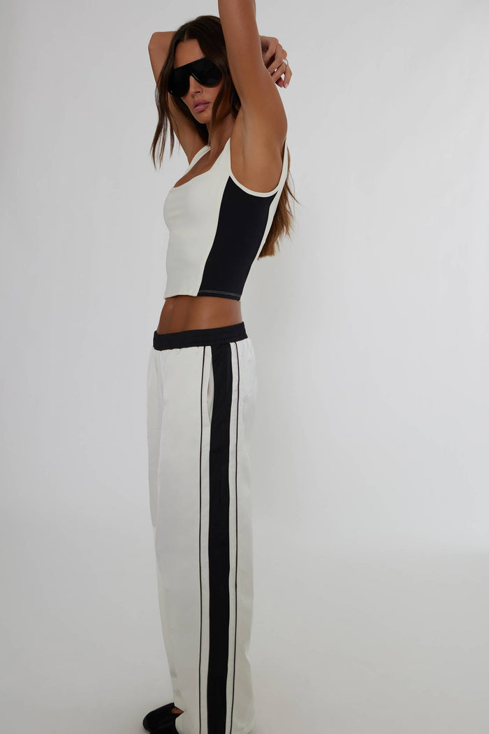 A woman modeling a matching two-piece knit set featuring a white crop top with black side panels and white wide-leg pants with black side stripes, set against a plain light gray background.