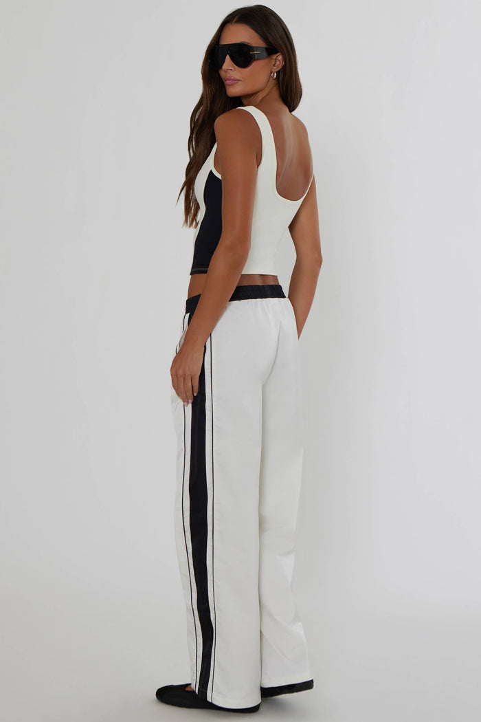 A woman modeling a white sleeveless crop top and matching white wide-leg trousers with black side stripes, shown from the back against a plain light gray studio background.
